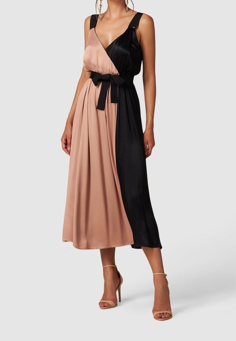 Femme portant une robe midi sans manches avec des blocs de couleur rose et noir, une ceinture noire à la taille et des sandales à talons beiges.