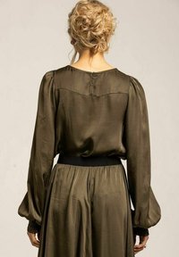 Olivgrön satinblus med puffärmar och svart elastisk midja, med knappstängning bak och slät yta.