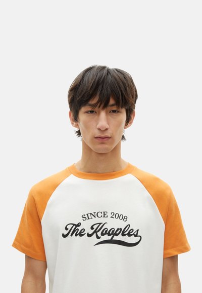 Weißes T-Shirt mit orangefarbenen Raglanärmeln, versehen mit dem "The Kooples"-Logo und dem Text "Seit 2008". Weicher Stoff mit einem lässigen Design.
