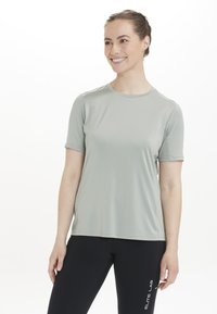 Lysegrøn atletisk T-shirt med korte ærmer, glat tekstur, rund halsudskæring, parret med sorte leggings med logodetaljer.