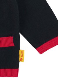 Manica e orlo in maglia nera con polsini a coste rossi e un'etichetta gialla con la scritta "Steiff" e il logo di un orsetto.