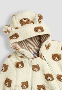 Giacca con cappuccio in pile cremoso caratterizzata da volti di orso bruno, design testurizzato, foderatura a righe e piccole orecchie sul cappuccio. Chiusura con zip frontale.