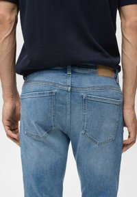 Jeans de mezclilla azul claro con una textura suave, corte recto y dos bolsillos traseros. Parche de cuero marrón en la cinturilla para marca.