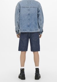 Vaaleansininen farkkutakki, jossa on väljä malli ja pitkät hihat. Yhdistetty tummansinisiin farkkushortseihin, joissa on näkyvät taskut, ja mustiin nilkkasaappaisiin.