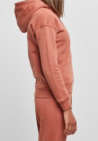 Sudadera con capucha en color rosa empolvado, hecha de una tela suave. Presenta puños y dobladillo acanalados, con un ajuste holgado.