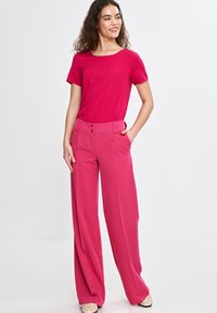 Fuksjowa bluzka z krótkim rękawem w zestawie z spodniami o wysokim stanie i szerokimi nogawkami w tym samym kolorze. Posiada dwa guziki w talii oraz kieszenie.