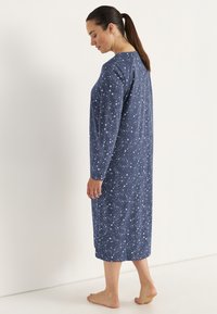 Mörkblå nattskjorta med långa ärmar, med ett vitt stjärnmönster, knä-lång, mjukt tyg och avslappnad passform.