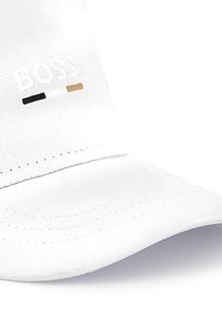 Witte katoen cap met geborduurd "BOSS" logo in witte, zwarte en gouden accenten, met een gebogen vizier en textiel met structuur.
