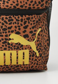 Ruksak s smeškom u smešku leopard uzorka u smešku sa žutim Puma logotipom i tekstom. Napravljen od tkanine s teksturiranom površinom i crnim patentnim zatvaračem.