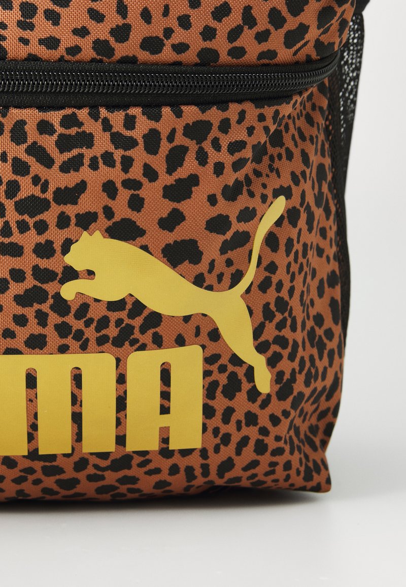 Mochila de tela con estampado de leopardo marrón que presenta un logo de Puma amarillo y texto. Fabricada con un material texturizado y con cremallera negra.