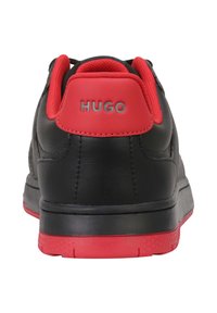 Sneakers en cuir noir avec un col rembourré et un onglet au talon rouges. Présente un logo gris au niveau du talon et une semelle extérieure en caoutchouc texturée.
