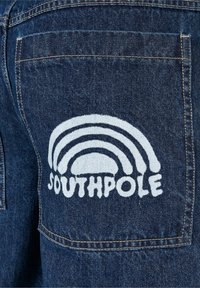 Poche en denim avec un motif imprimé blanc de trois formes d’arche au-dessus du mot « SOUTHPOLE » en lettres grasses.