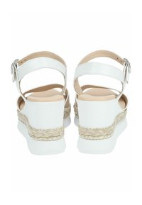 Sandales compensées blanches avec une semelle en jute tressé. Elles sont dotées d'une large sangle de cheville et d'une boucle en argent. Texture en cuir lisse. Semelle intérieure neutre.