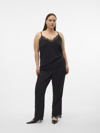 Camisole noire avec bordure en dentelle, assortie à un pantalon noir avec des accents en dentelle à l'ourlet. Le mannequin est debout devant un fond blanc uni.