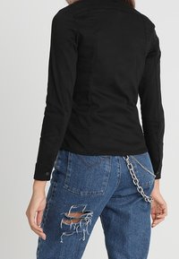 Svart långärmad skjorta med en figurnära design, i kombination med blå slitna jeans med rivna detaljer och en silverkedja som accent.