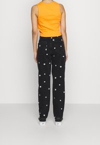 Černé džíny s bílými květinovými ozdobami, rovný střih, vysoký pas. Kombinované s oranžovým bezrukávovým topem. Bílé tenisky.