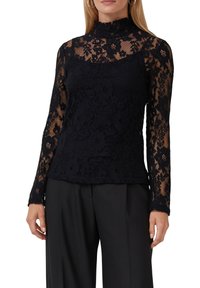 Haut noir en dentelle à manches longues avec un col montant, présentant des motifs floraux et une texture semi-transparente. Associé à un pantalon noir ajusté.