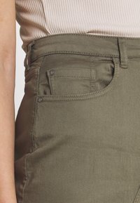 Pantalons vert olive en tissu doux, dotés d'une taille standard, de poches avant et de détails de couture visibles.