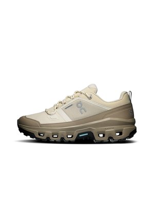 Light beige and brown waterproof trail running shoe with thick treaded sole and loop pull tab at heel, side logo visible.