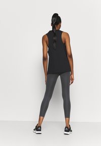 Černý bezrukávový top a šedé legíny. Top má jednoduchý design, zatímco legíny jsou přiléhavé a hladké. Černé sportovní boty.
