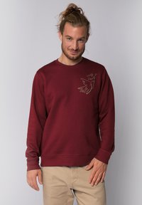 Maroon sweatshirt with crew neck, long sleeves, and a fitted hem. Features a bird illustration and the text "self love" in a subtle design.