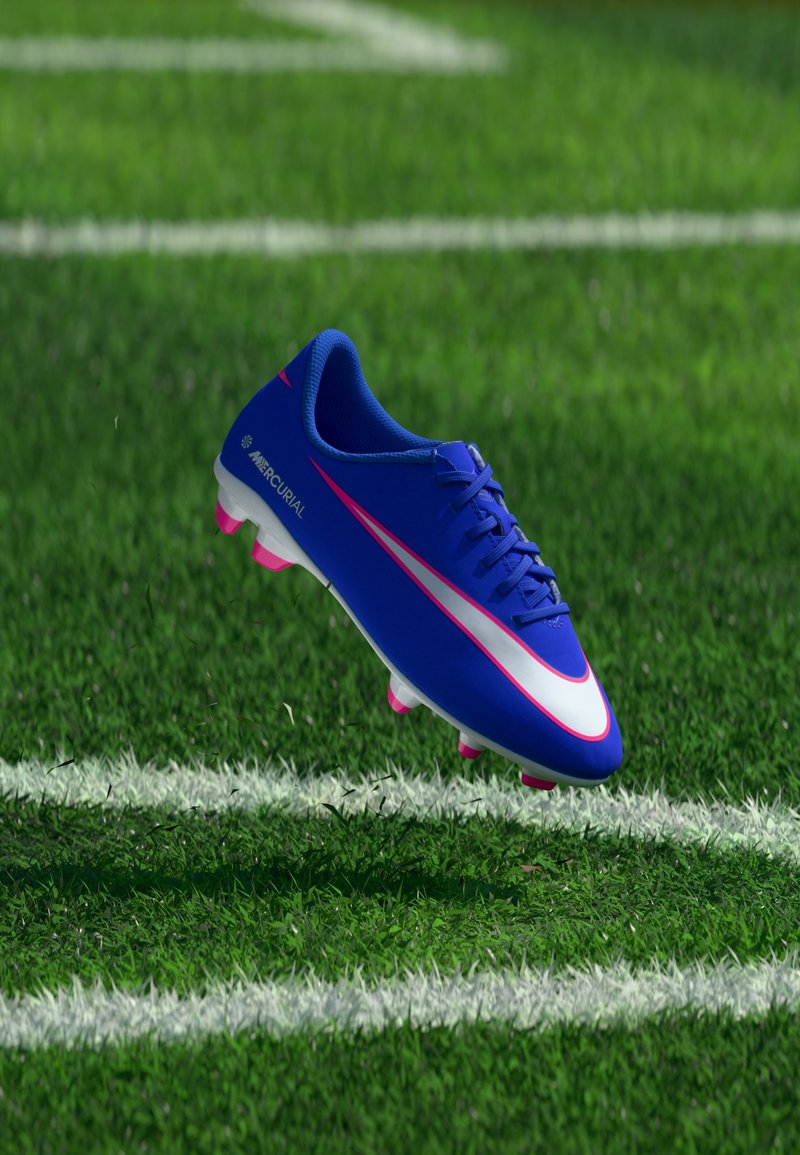 Crampon de football Nike Mercurial bleu avec des crampons roses flottant au-dessus de l'herbe verte près des lignes blanches du terrain.