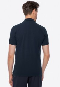 Tmavě modré polo tričko, krátké rukávy, klasický límec, texturovaná látka, boční rozparky na spodním lemu, rovný střih, viditelné detaily šití.