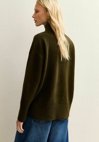 Dunkelgrüner, übergroßer Rollkragenpullover aus weichem Stoff, mit gerippten Bündchen und Saum, kombiniert mit weiten blauen Jeans.