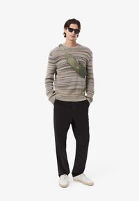 Maglione lavorato a maglia con strisce multicolori, borsa a tracolla verde oliva, pantaloni neri e sneakers bianche. Tessuto liscio e vestibilità rilassata.