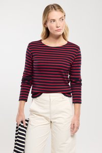 Marineblå og rødstribet langærmet skjorte med rund hals, båret med hvide bukser, der har en afslappet pasform og blød stoftekstur.