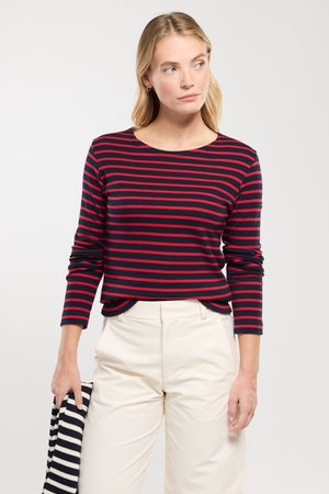 Gestreiftes Langarmshirt in Marineblau und Rot mit Rundhalsausschnitt, getragen mit weißen Hosen, featuring eine lockere Passform und weichen Stofftextur.