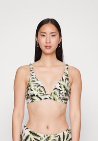 Top de bikini com padrão floral e decote profundo. Apresenta alças largas, padrões de folhas verdes e pretas sobre um fundo claro. Textura de tecido suave.