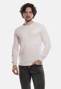 Maglione bianco a maglia testurizzata con scollatura a girocollo e maniche lunghe, abbinato a jeans scuri. La vestibilità è morbida e il tessuto sembra essere soffice.