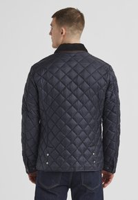 Navy gefütterte Jacke mit einem Cordkragen, Druckknopfdetails und strukturiertem Rautenmuster in einem leichten, gepolsterten Design.