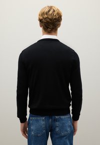 Schwarzer Pullover mit langen Ärmeln und rundem Halsausschnitt, von hinten betrachtet. Getragen mit ausgewaschenen blauen Jeans. Glatte Textur.