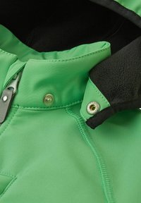 Veste softshell verte avec doublure en polaire noire, dotée d'un zip sur le devant, d'une fermeture à snap, et d'accentuations cousues sur le col et le corps.