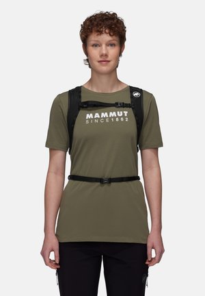Person trägt ein olivgrünes Mammut-T-Shirt und einen schwarzen Klettergurt-Rucksack, schaut nach vorne vor neutralem Hintergrund.