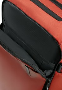 Zaino rosso aperto che mostra il compartimento per laptop imbottito in nero e i dettagli interni con chiusura a zip.