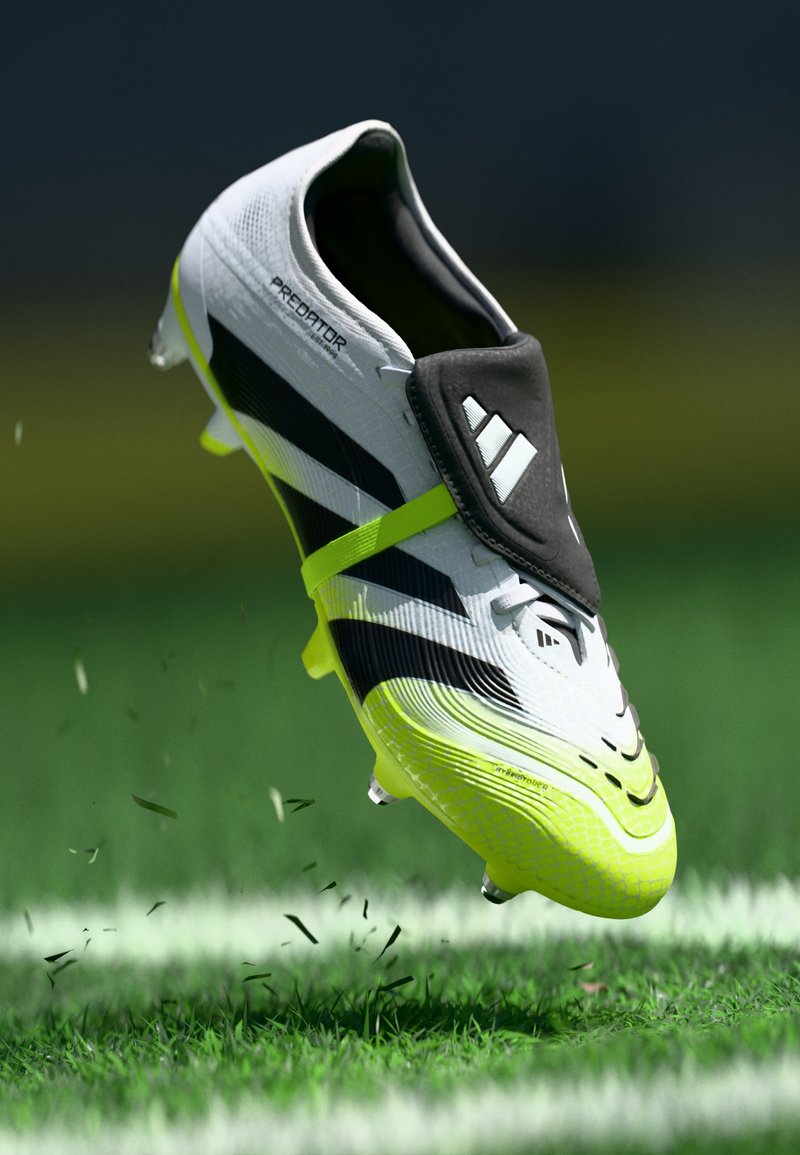 Crampons de soccer noirs et blancs avec une surface texturée, dotés d'accents jaunes vifs et d'un col type chaussette noir, montrés en l'air sur de l'herbe.