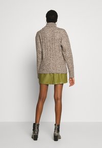 Maglione marrone a maglia con colletto alto, caratterizzato da un motivo testurizzato, abbinato a una mini gonna verde oliva lucida e stivali alla caviglia con motivo a serpente.