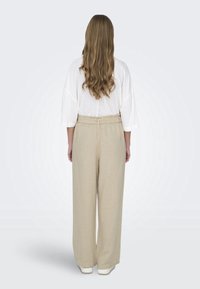 Krémové lněné kalhoty širokého střihu s nařaseným pasem, doplněné o volnou bílou blůzu s širokými rukávy, zobrazené zezadu.