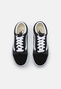 Zapatillas de ante negro con cordones blancos y acentos laterales. Punta redondeada y suela plana con borde blanco. El interior presenta un forro beige.
