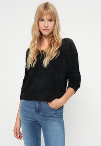 Fekete, texturált pulóver széles nyakkivágással és háromnegyedes ujjakkal, kék skinny farmernadrággal párosítva. Egyszerű dizájn és laza fazon.