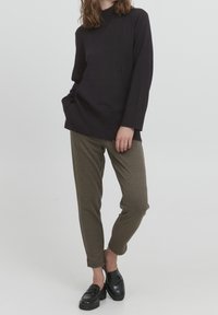 Maglietta nera a maniche lunghe con colletto alto, abbinata a pantaloni a gamba affusolata a quadri marrone e mocassini neri. Design semplice, texture liscia.