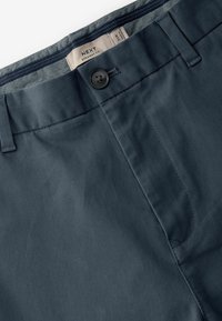 Pantalones rectos en color marino hechos de una tela suave, con cierre de botón y cremallera. Presentan costuras sutiles y un cinturón interior con un estampado.
