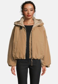 Lichte, beige, gewatteerde bomberjack met een hoge kraag, rits aan de voorkant en zijzakken. Beschikt over elastische manchetten en een relaxed fit.