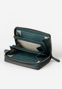 Portafoglio in pelle teal con chiusura a zip. Caratterizzato da più scomparti per carte, due compartimenti e foderato in tessuto a righe. Accentato da hardware in bronzo.