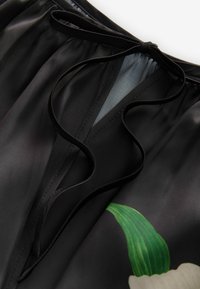Vêtement en satin noir avec des détails de motif floral. Dispose d'une fermeture à nouer au niveau du col, d'une texture douce et d'une drapé fluide.