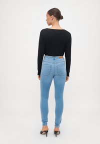 Svart langermet topp med ribbestruktur, kombinert med lyseblå skinny jeans med baklommer og en beige lærlabel i midjen.