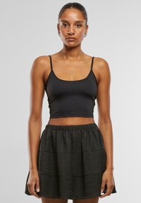 Zwart cropped tanktop met dunne bandjes, gecombineerd met een zwarte, gelaagde minirok met een elastische tailleband en een gestructureerde stof.
